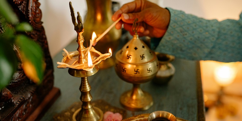 A person igniting the incense stick and a brass diya for aarti and pooja on the table.