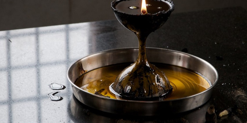 Oil diya with burning jyoti placed on a silver plate with oil near burnt incense