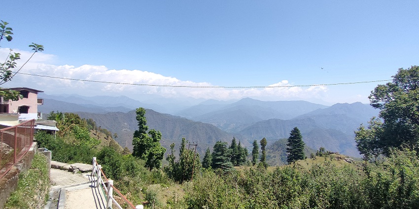A view of Patal Bhuvaneshwar, showcasing green hills and a cloudy sky in the background.
