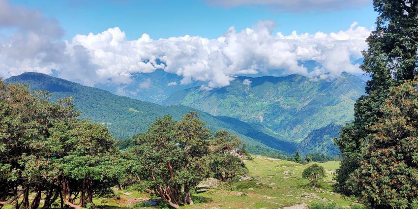 Scenic view of Pauri Garhwal with lush hills, scattered houses, and Himalayan backdrop.