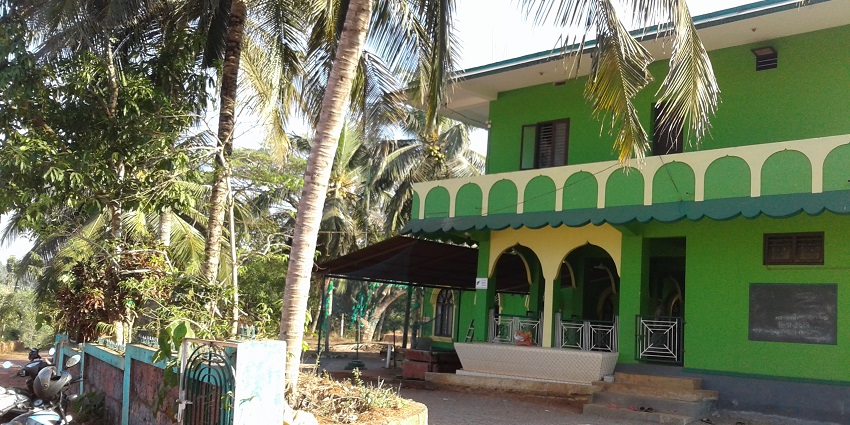 A picture of the entrance of a dargah with green painted walls and a small garden in front