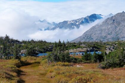 A scenic view of Alaskan sky, highlands and mountains covered with clouds