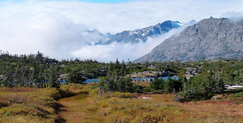 A scenic view of Alaskan sky, highlands and mountains covered with clouds