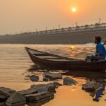 An oarsman sits on his boat at sunset on river Damodar on a foggy winter afternoon.