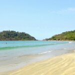 A serene beach in Goa, showcasing golden sands and clear blue waters under a sunny sky.