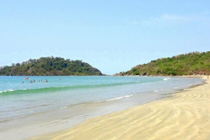 A serene beach in Goa, showcasing golden sands and clear blue waters under a sunny sky.