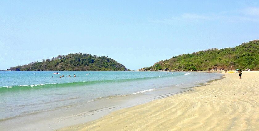 A serene beach in Goa, showcasing golden sands and clear blue waters under a sunny sky.