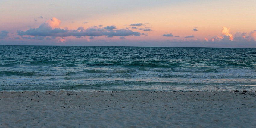 Poompuhar Beach with sandy shores and waves crashing under a cloudy coastal view.