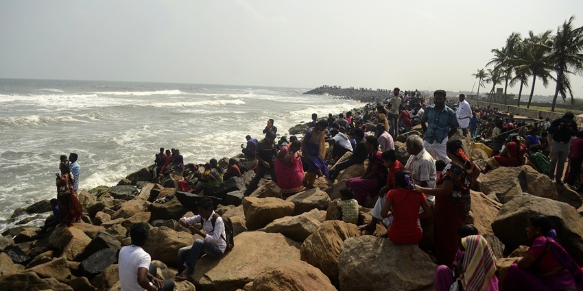 A group of people gathered and sat on the rocks at the shore of the Poompuhar beach