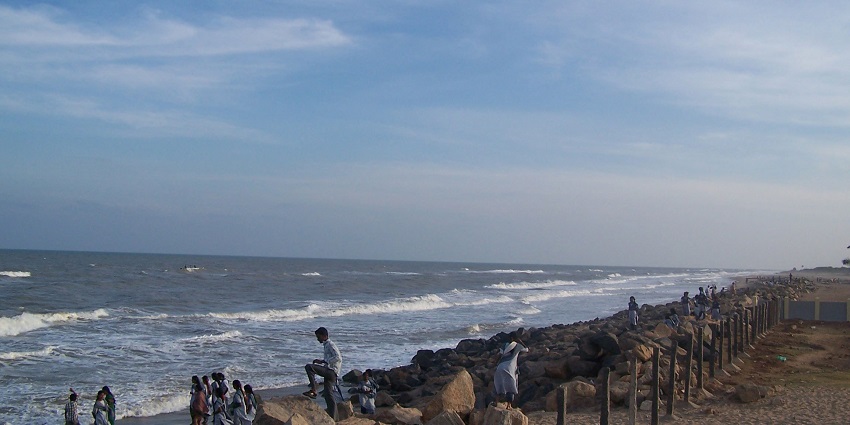 People at the Poompuhar beach with bordered rocky land and gentle waves hitting the shore.