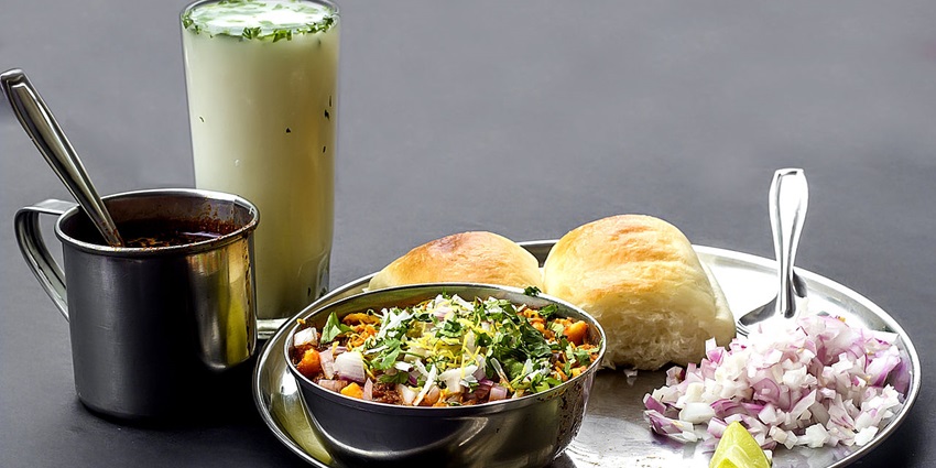 Spicy Kolhapuri misal served with two slices of bread, chopped onions and lime wedge
