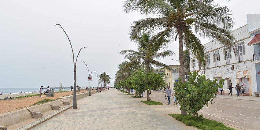 Promenade along Puducherry Beach with palm trees, benches, street lamps, and people