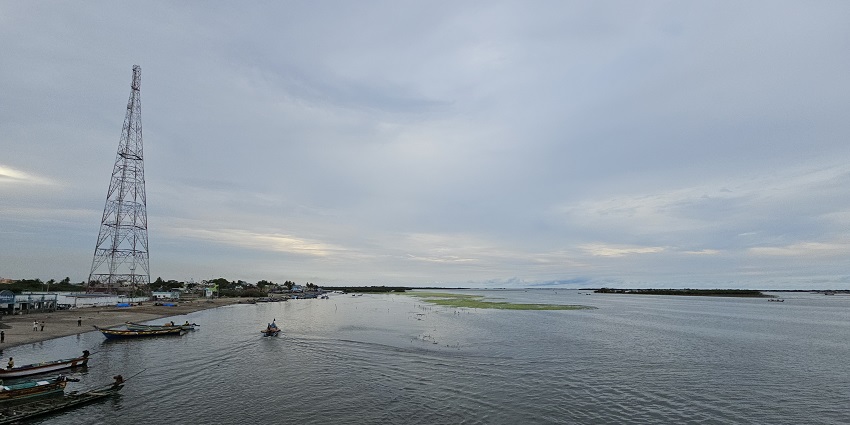 Pulicat Lake with calm water, moving and parked boats with a tall tower in the background