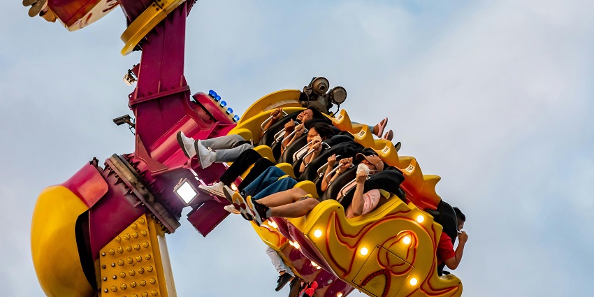 An image of a bright red roller coaster with riders enjoying the thrill set against a clear blue sky.