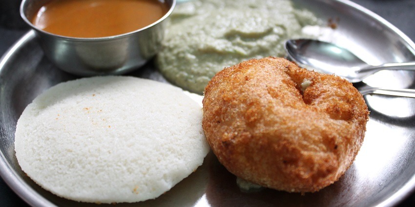 Several pieces of Rava Idli are served on a leaf alongside Sambar and Coconut Chutney