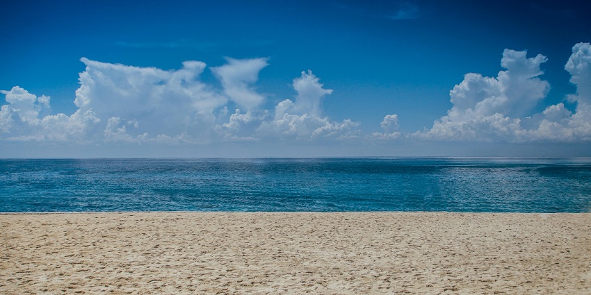 A scenic ocean view during daylight, showcasing clear blue waters, gentle waves, and a bright sky.