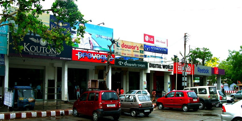 Bustling Sadar Bazar street in Agra lined with shops, goods, and shoppers at midday
