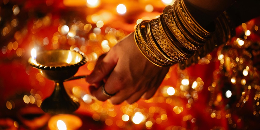 A woman lighting diya at a temple, the surroundings being illuminated by golden light.