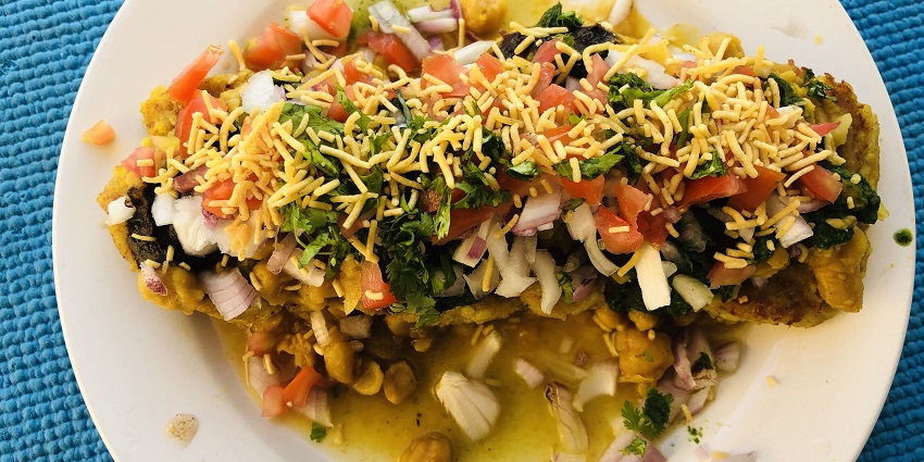 A top view of vibrant ragda patties topped with sev are served on a white platter.
