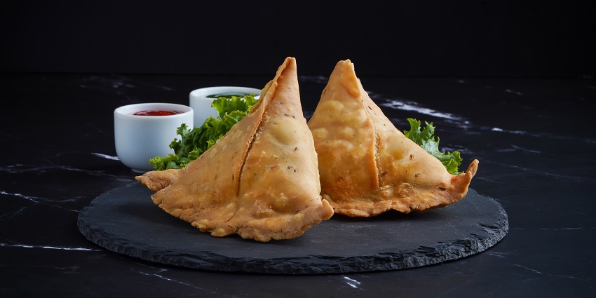 A picture of a plate decorated with Samosas cut in half, served with a tangy tamarind dip