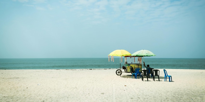A woman walking on the Sankaranainar Kovil Beach, with golden sands and gentle waves, creating a peaceful atmosphere.