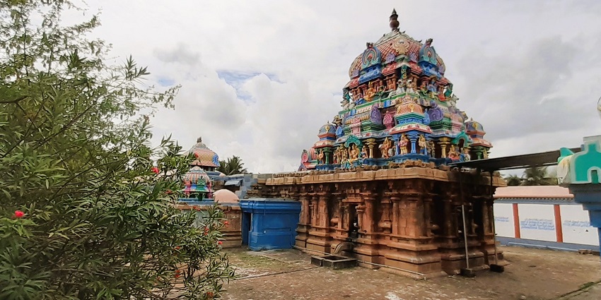 A vibrantly coloured temple with stone carvings around which other structures are present.