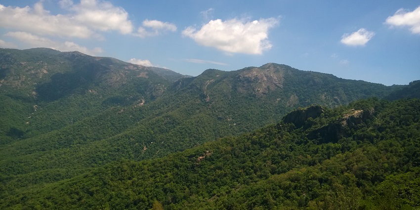 Kolli Hills viewpoint with green forested hills, rocky outcrops, and a partly cloudy sky.