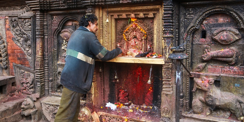 A man standing near an intricately carved stone shrine in Coimbatore performing a ritual.