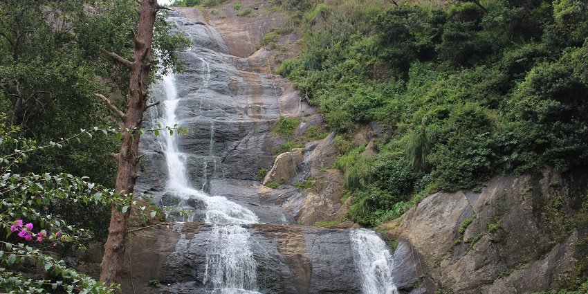 Silver Cascade Waterfall flowing down rocky cliffs with people around clicking pictures.