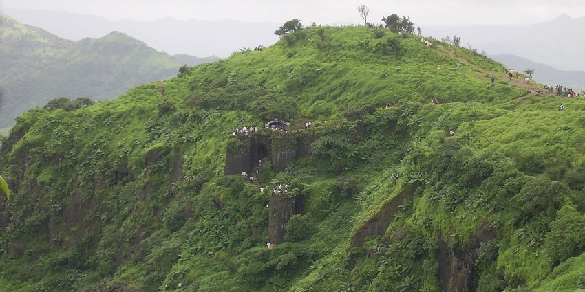 A scenic picture of Sinhagad Fort's ruins on a hilltop surrounded by mist and greenery.