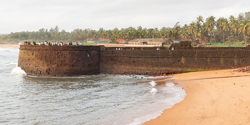 Wide angle view of the Sinquerim Fort on a sandy shore, with the waves crashing its walls.