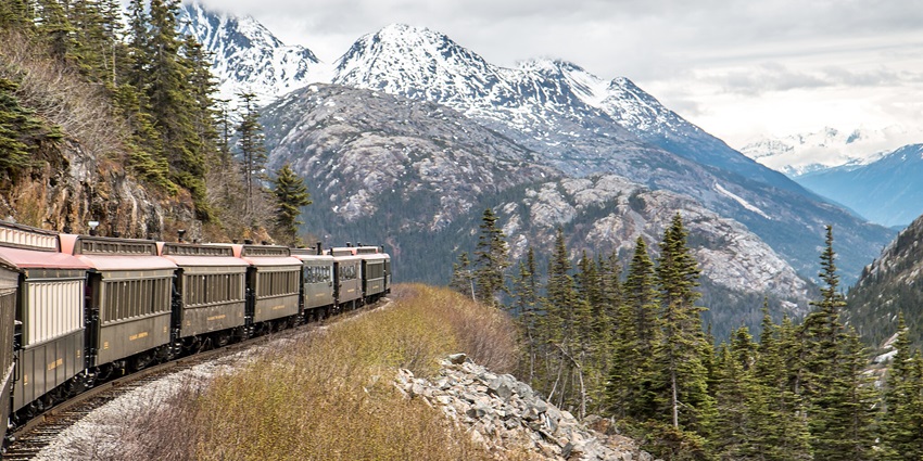 A train going through the White Pass on the Yukon railroad flanked by mountains and trees.