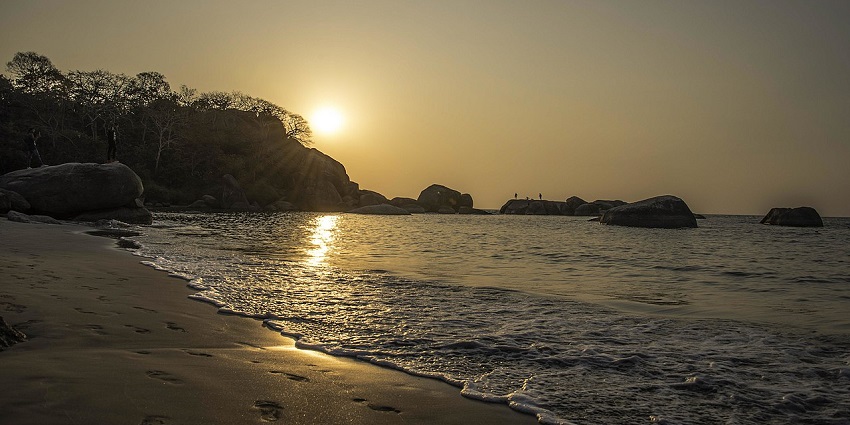 A serene stretch of golden sand flanked by green hillocks, with turquoise sea waves lapping the shore at Bhandarpule Beach, one of the best things to see in Ganpatipule.
