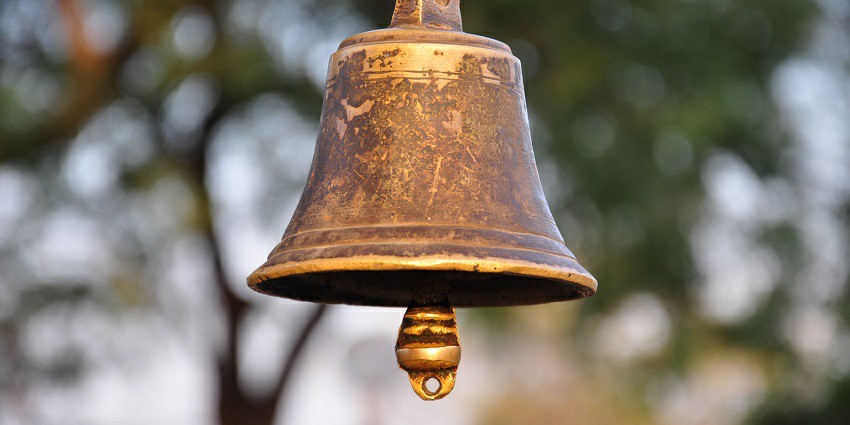 Ancient metal bell hanging in the Thousand Pillar Temple, framed by intricate stone carvings