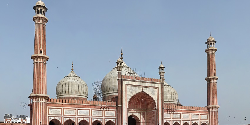 A picture of Jama Masjid with a huge dark brown circular structure with big towers and spires.