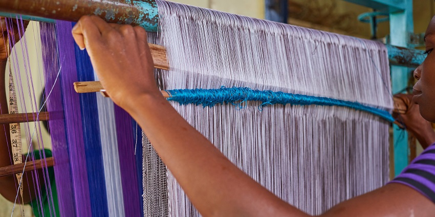 A picture of a woman weaving clothes on a handloom