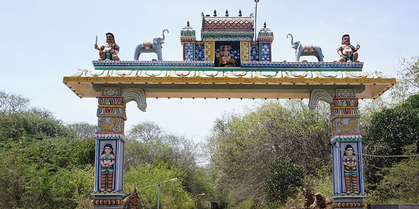 Temple entrance arch with intricate carvings and vibrant colours surrounded by greenery.