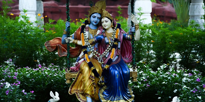 Two statues on a swing, surrounded by greenery, creating a serene outdoor setting