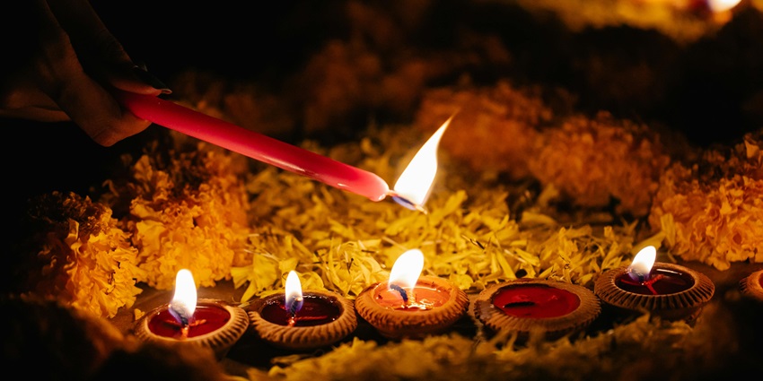 A person lighting candles at a Temple in Virar, with multiple candles glowing in the foreground.