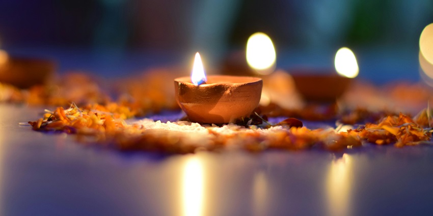 A close-up of a brown scented candle with a flame, placed on a wooden surface.