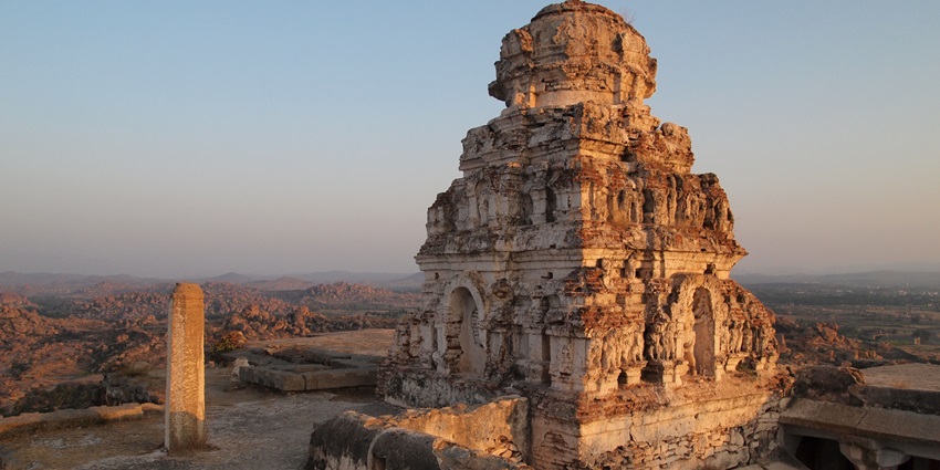 Ancient stone shrine atop a rocky hill, overlooking a vast landscape under a clear sky.