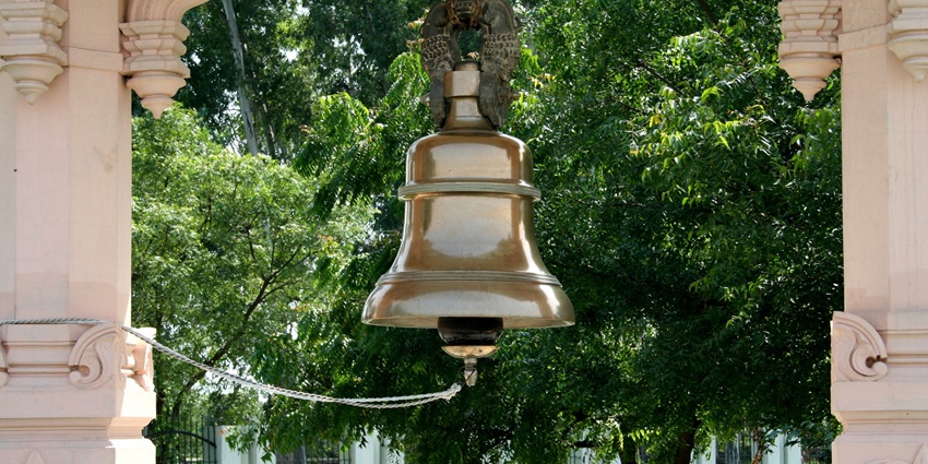 A close-up of a brass temple bell hanging from a wooden frame, used in Hindu rituals