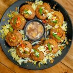 A glimpse of pani puri beautifully decorated and served on a black plate on a table.