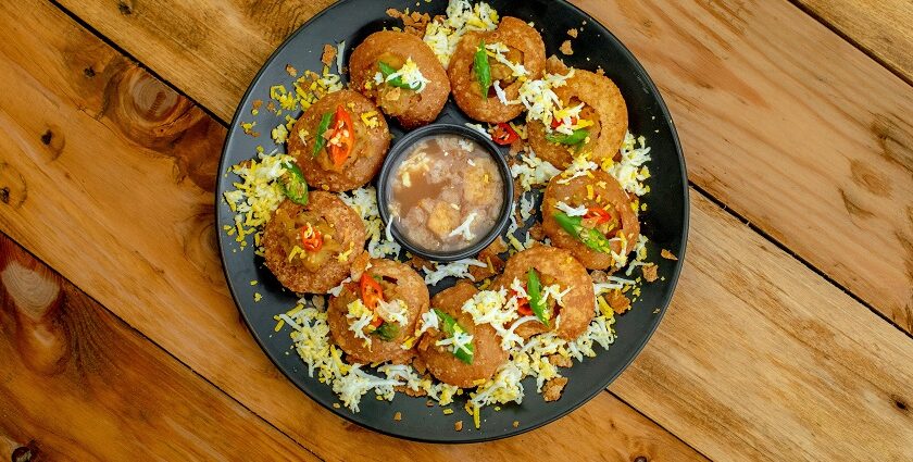 A glimpse of pani puri beautifully decorated and served on a black plate on a table.