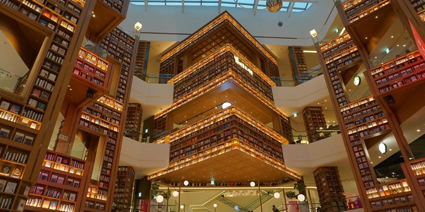 Spacious modern library with towering bookshelves and a glass roof, flooded with natural light