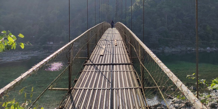 A glimpse of the Suspension Bridge over blue waters surrounded by greenery.