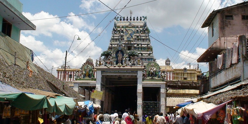Swamimalai Murugan temple is on a street with local shops on both sides and devotees visiting.