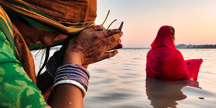 Two women dipping in water and praying to lord Surya with hands in namaskar position