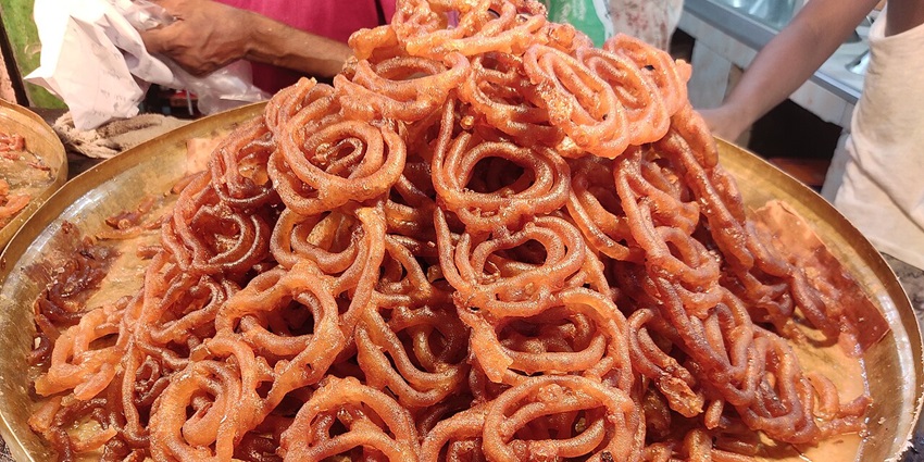 Close-up of freshly made jalebi sweets stacked on a tray, golden and syrup-soaked