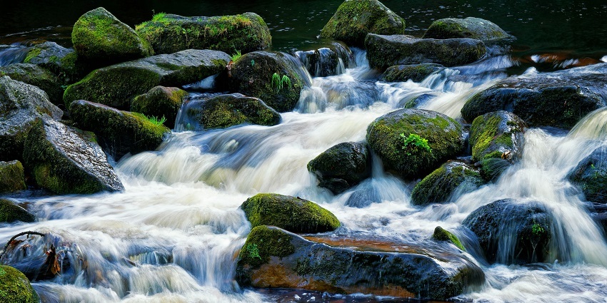 An image of Tanda Falls where water is seen running over rocks which have grass growing.